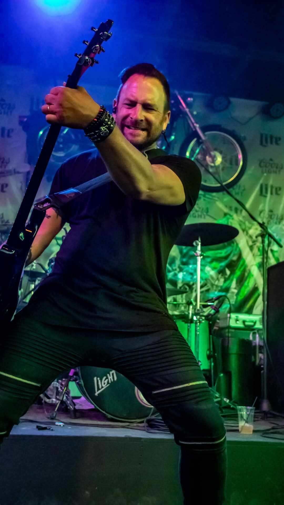 Bass player mid-riff under blue and green stage lights