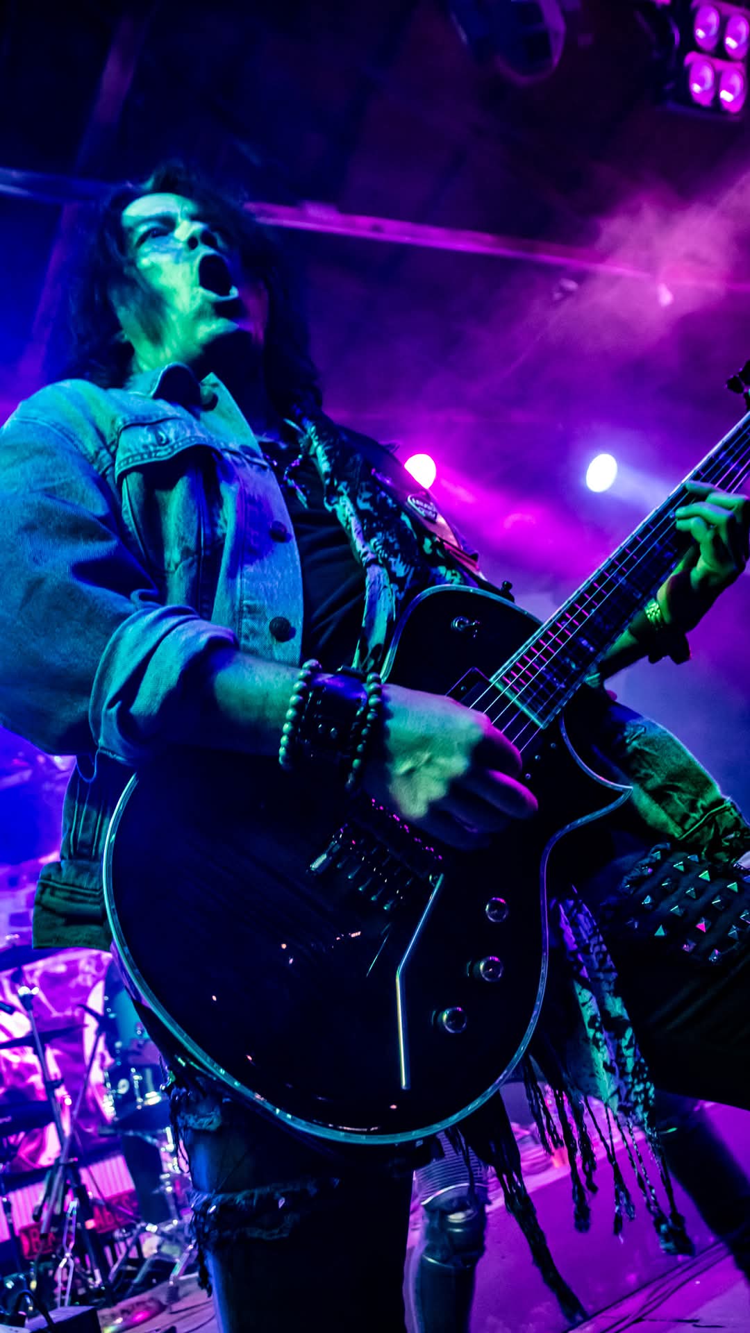 Guitarist mid-solo bathed in purple and green light