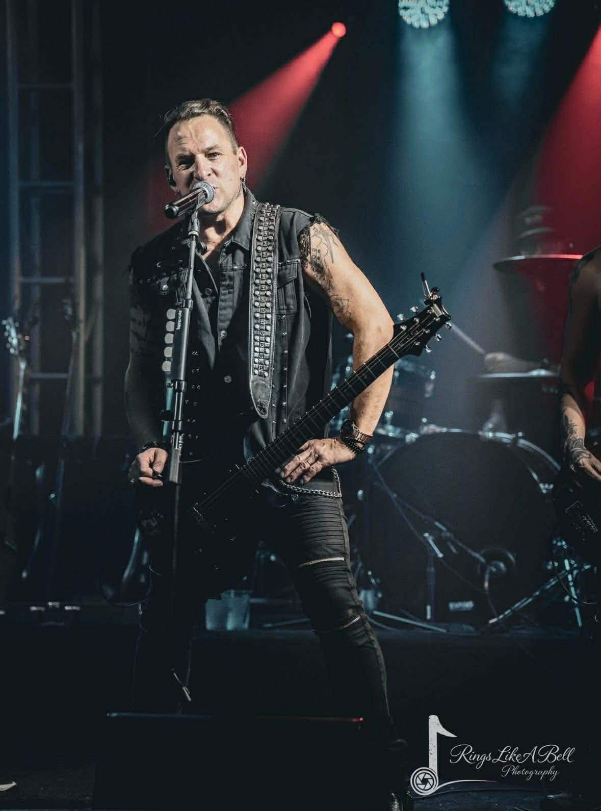 Lead vocalist with studded vest and guitar at the mic under red light