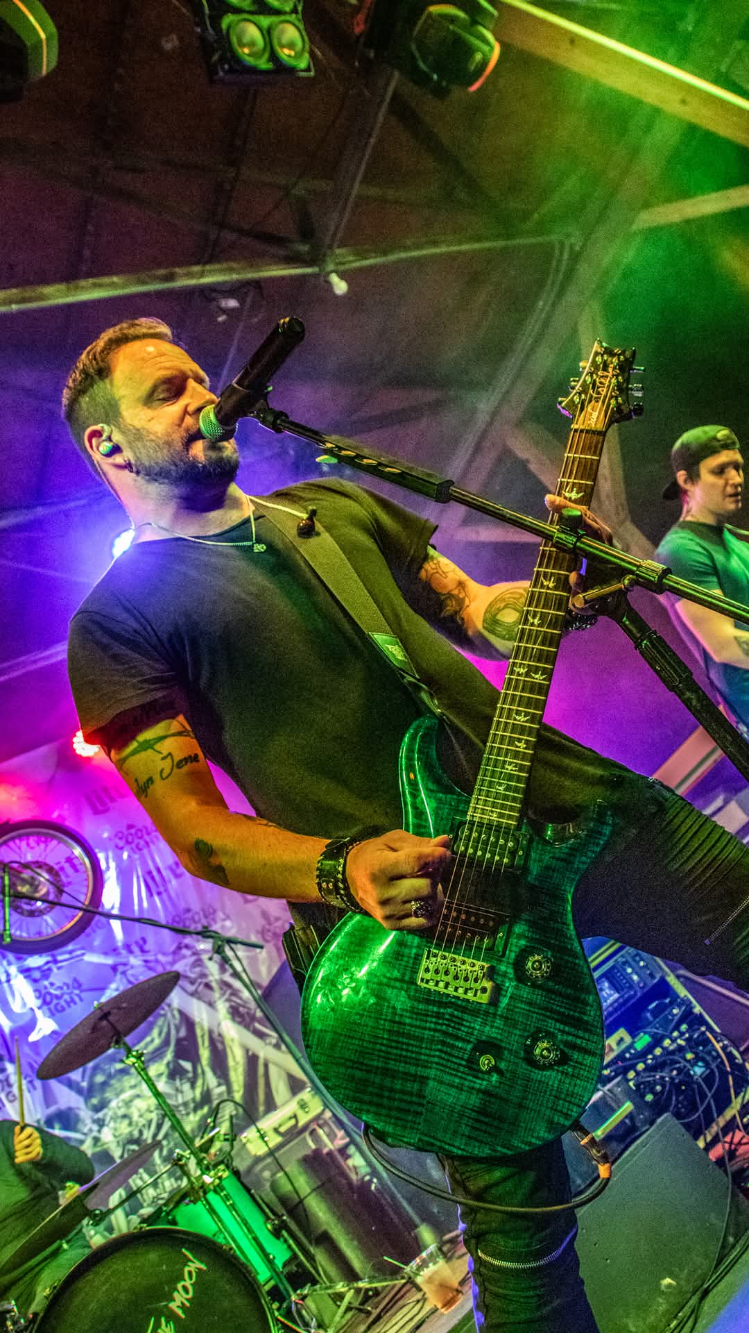 Guitarist with green PRS singing into the mic under purple and green lights