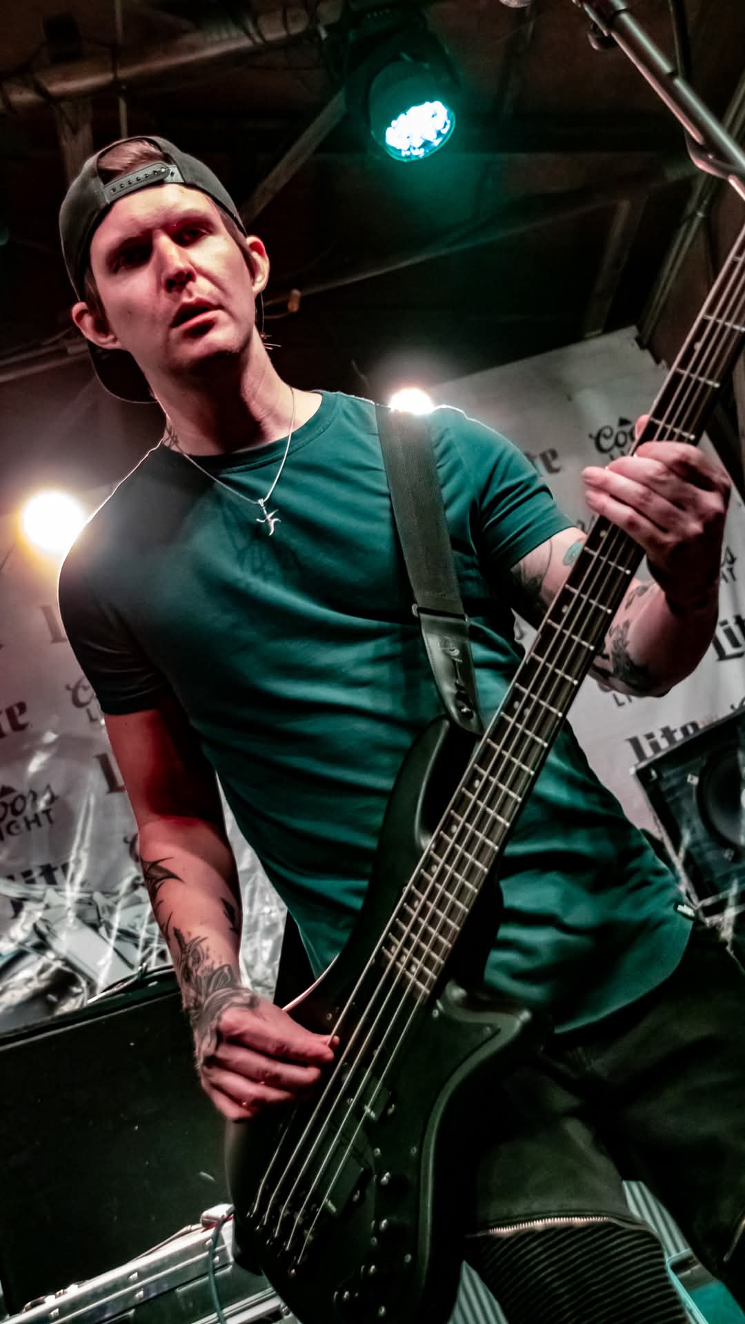 Bassist mid-riff in green shirt under teal stage light
