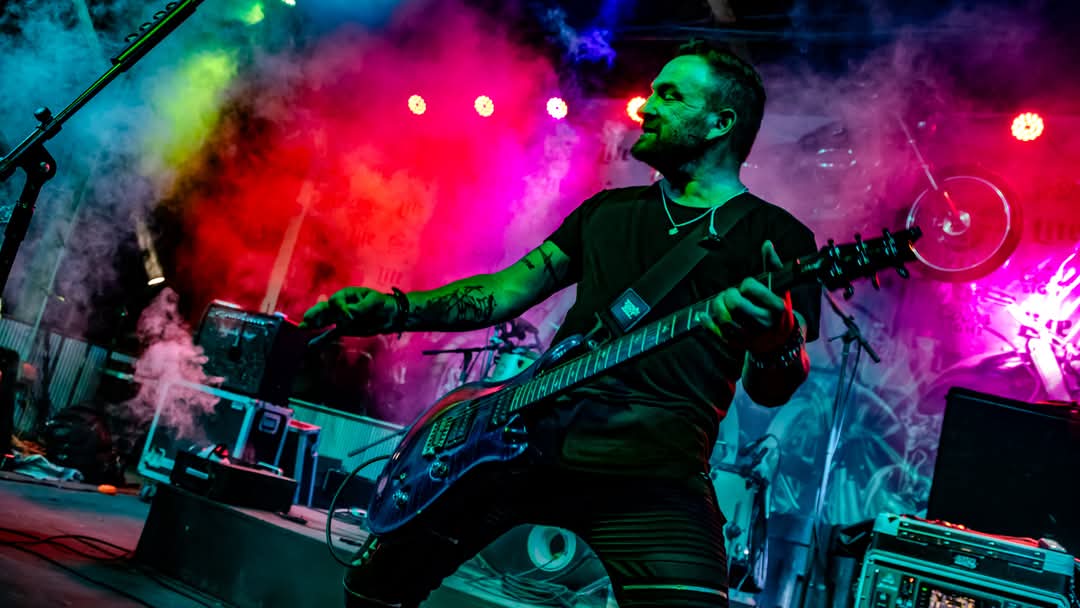 Guitarist mid-riff surrounded by red and pink smoke