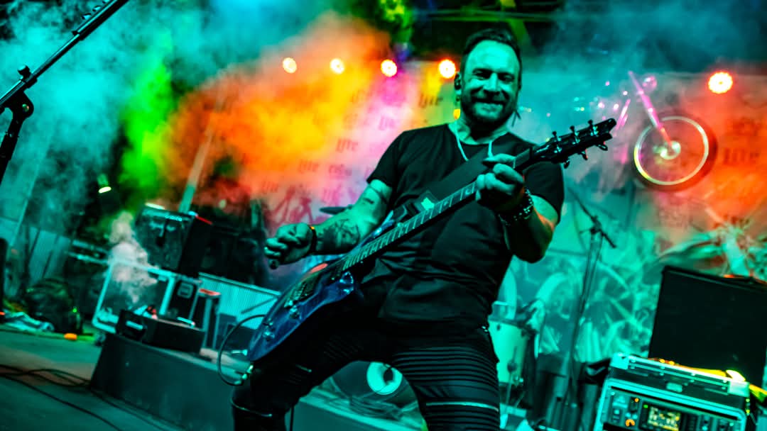 Guitarist smiling mid-performance with colorful smoke behind